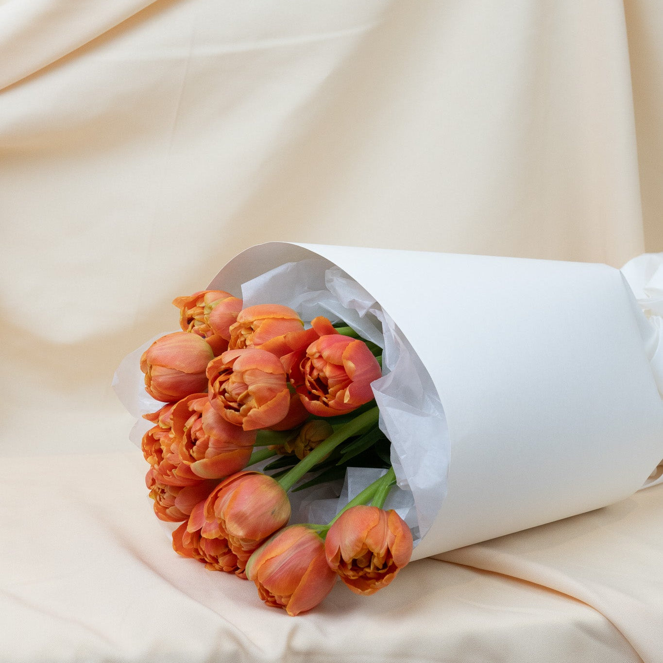 Bouquet of orange tulips wrapped in white paper on a beige fabric background
