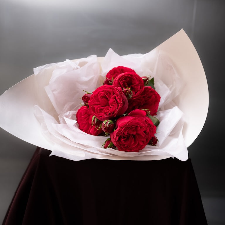 Bouquet of red roses wrapped in white paper on a dark surface with a gray background