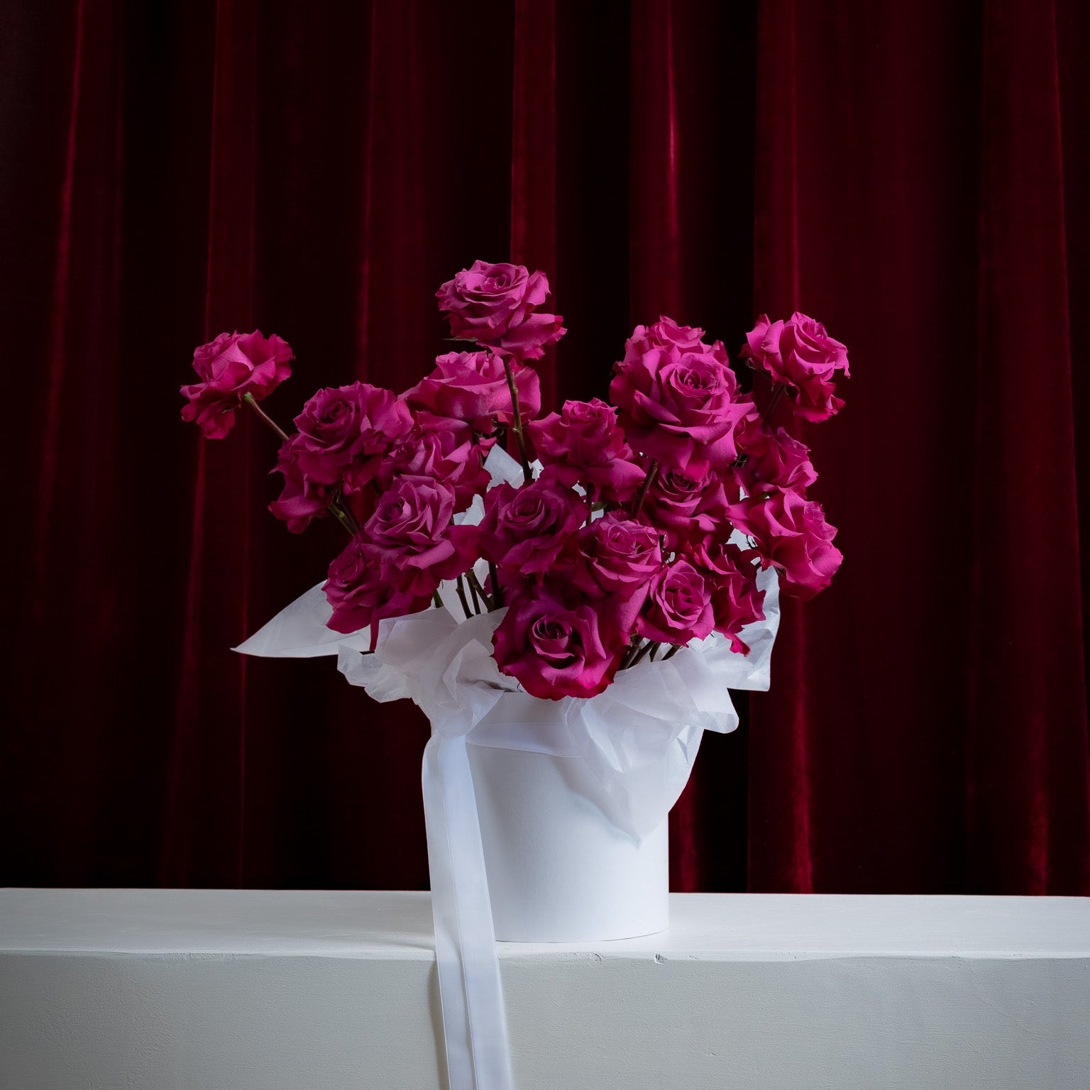 Bouquet of pink roses wrapped in white paper on a white surface with a red curtain background